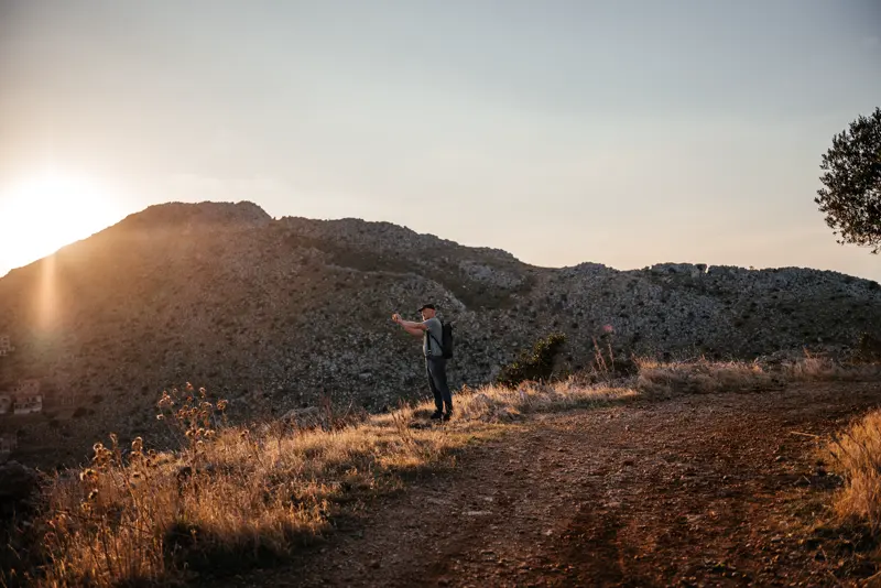 A hiker on the Capo Gallo trail at sunset with the hillside behind